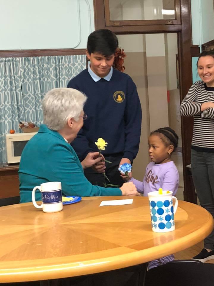 A child brings a flower to Sister Rita Marie on Principal Appreciation Day, 2018.