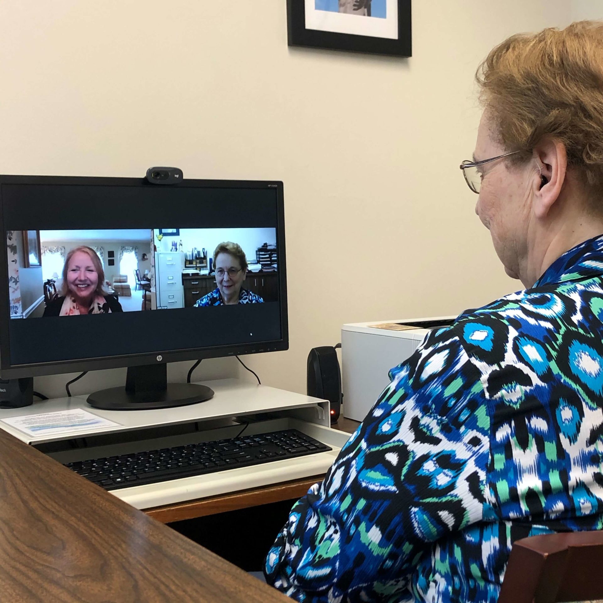 Sr Marilyn Jean Runkel sitting at her desk chatting with two women via Zoom videoconference